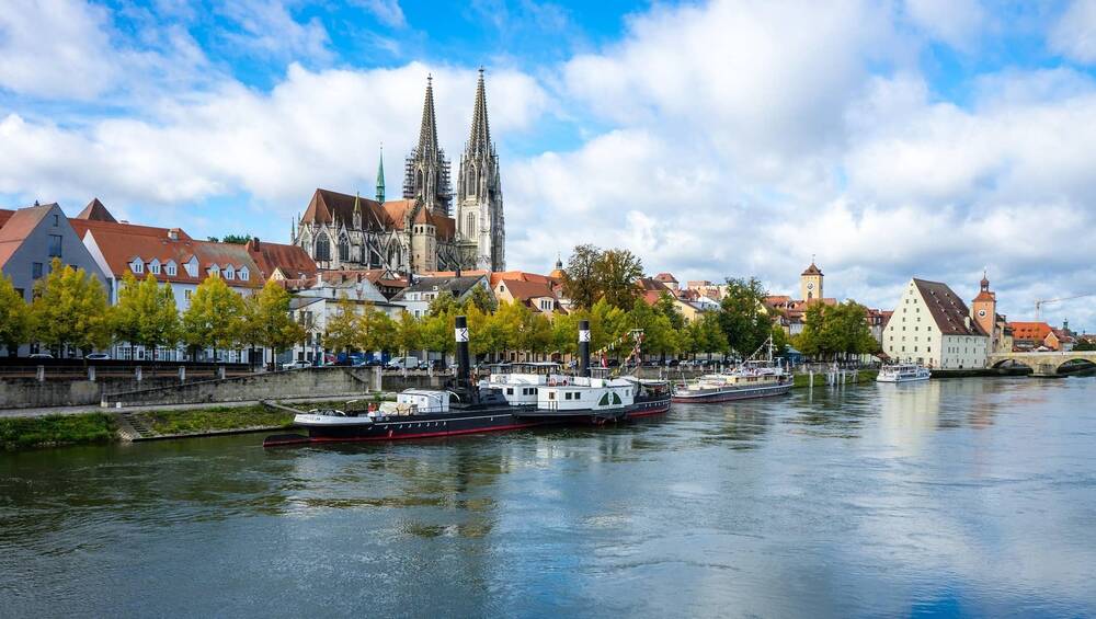 Blick auf die Altstadt von Regensburg an der Donau, mit historischen Gebäuden und Schiffen im Wasser.